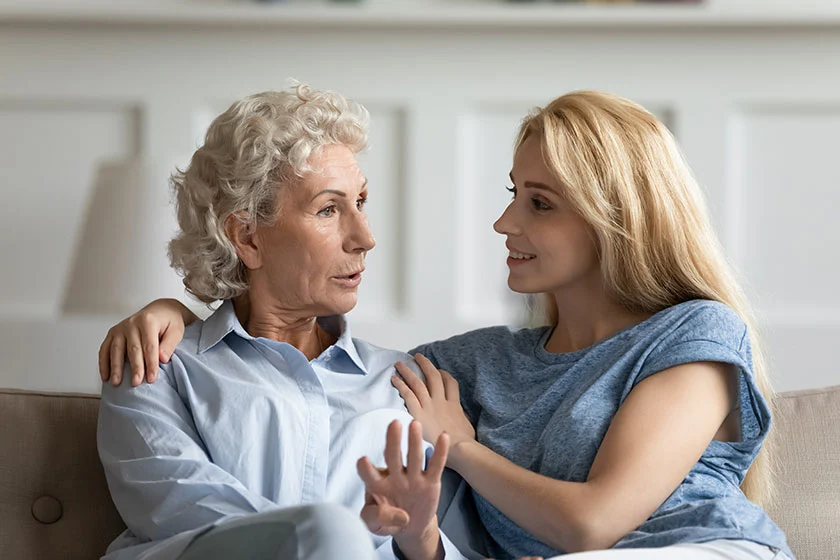 An older mother and adult daughter having a relaxed conversation at home